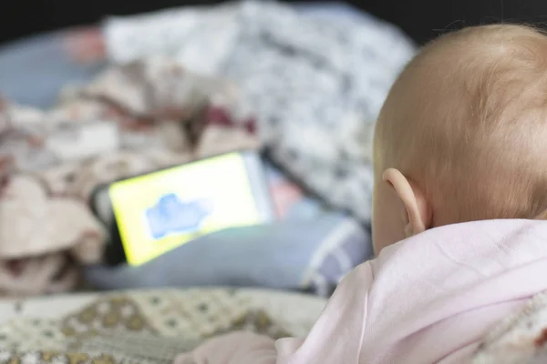 小さな赤ちゃんがソファに横たわって 電話で漫画を見ている ストック写真
