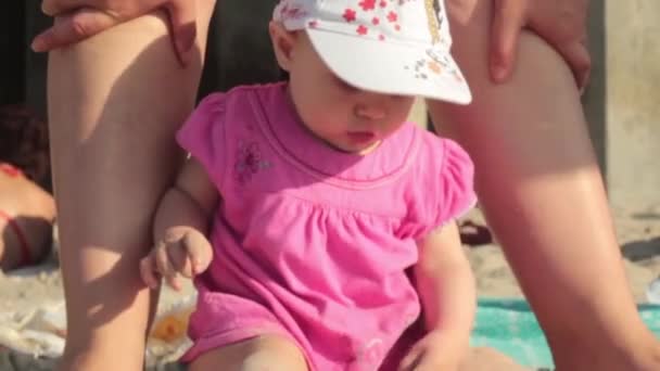 A little girl in a red dress sitting on the sand on the beach — Stock Video