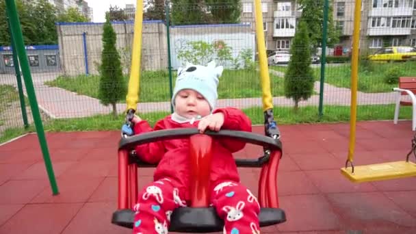 Una niña pequeña con una chaqueta roja montada en un columpio — Vídeo de stock