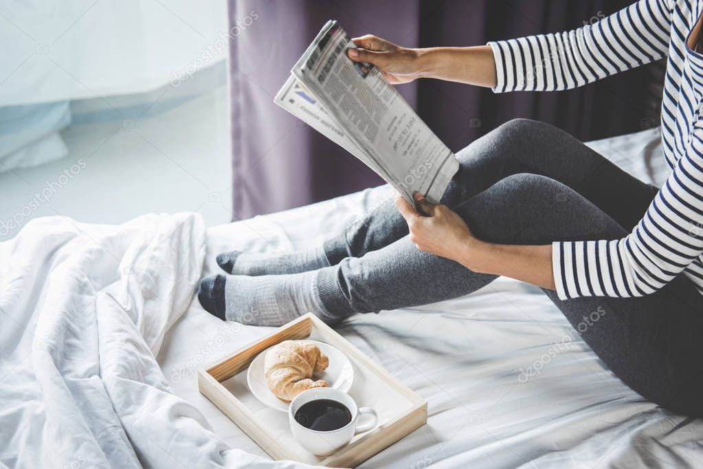 Relaxation and recreation, Young happiness woman on the bed with enjoying reading newspaper in holiday and morning cup of coffee and Croissant.
