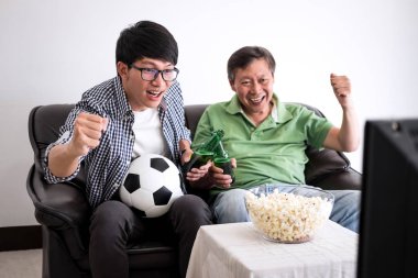 Genç Asyalı adam ve baba futbol spor ve eğlence kavramının tv ve bira ve patlamış mısır vasıl ev ile kutluyor tezahürat futbol takımı maç izlerken.