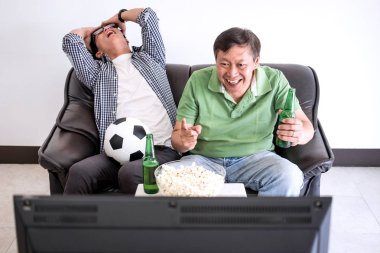 Genç Asyalı adam ve baba futbol spor ve eğlence kavramının tv ve bira ve patlamış mısır vasıl ev ile kutluyor tezahürat futbol takımı maç izlerken.
