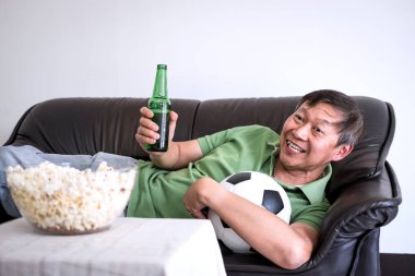 Spor ve eğlence kavramının tv ve bira ve patlamış mısır vasıl ev ile kutluyor tezahürat futbol takımı maç futbol izlerken Genç Asyalı adam fanclub.