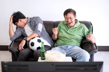 Genç Asyalı adam ve baba futbol spor ve eğlence kavramının tv ve bira ve patlamış mısır vasıl ev ile kutluyor tezahürat futbol takımı maç izlerken.