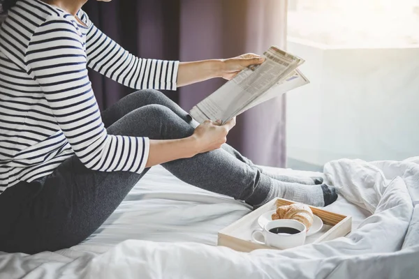 休闲娱乐 年轻快乐的女人在床上享受阅读报纸在假日和早晨的咖啡和牛角面包 — 图库照片
