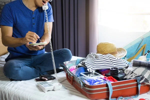休日の旅行や旅の旅行に備えて旅行や休暇の概念は スーツケースはベッドの上に彼の衣服および原料の多くを梱包幸福若い男 — ストック写真