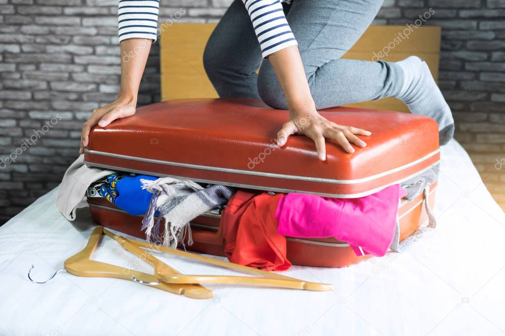 Travel and vacation concept, happiness young woman packing a lot of her clothes and stuff into suitcase on bed prepare for travel and journey trip in holiday.
