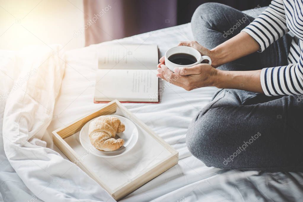 Relaxation and recreation, Young happiness woman on the bed with old book and morning cup of coffee in hands and Croissant.