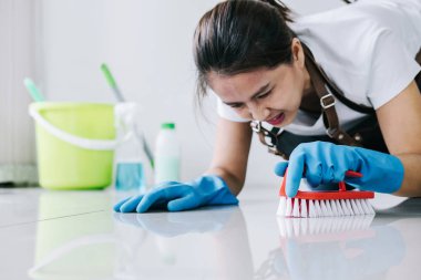 Kat Hizmetleri ve kavramı, mutlu genç kadın mavi kauçuk eldiven toz katta evde temizlerken bir sprey ve bir fırça kullanarak silerek Temizleme.