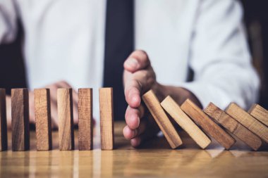 İş dünyası için strateji ve başarılı müdahale kavramı, iş adamı eli Devrilen tahtadan Domino taşları sürekli devrilmezse risk almayacak.