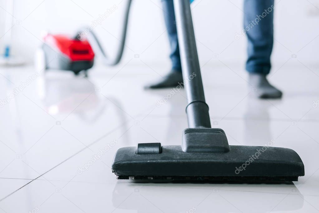 Housekeeping and housework cleaning concept, Happy young man in blue rubber gloves using a vacuum cleaner on floor at home.
