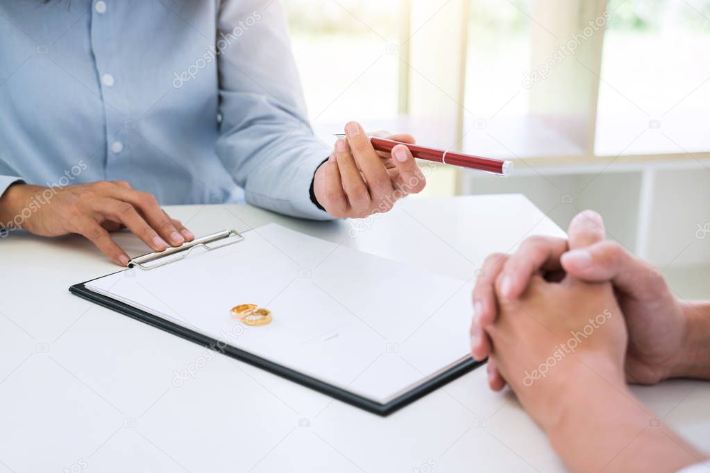 Husband and wife are reading divorce agreement and filing pen to signing decree of divorce (dissolution or cancellation) of marriage filing divorce papers and two golden marry ring.
