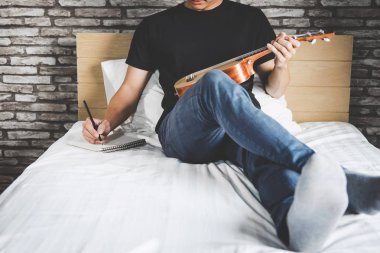 Genç mutluluk müzik zevk yatak odası adamım ve bir şarkı gitar ya da tatil, dinlenme ve Rekreasyon kavramı içinde ukulele ile yazmak.