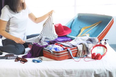 Seyahat ve tatil kavramı, mutluluk genç kadın elbiselerini ve malzeme bir sürü bavul yatak içine ambalaj tatil seyahat ve yolculuk yolculuk için hazırlamak.