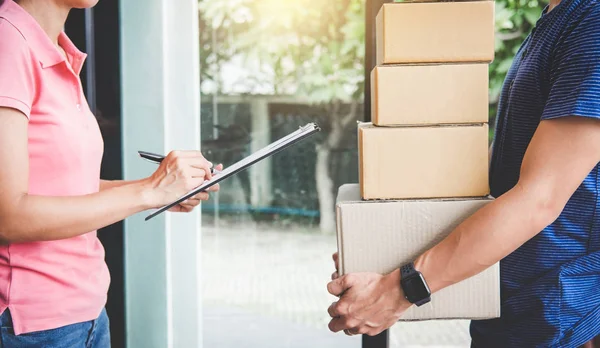 Home delivery service and working with service mind, Woman customer signing and receiving a cardboard boxes parcel from deliveryman.