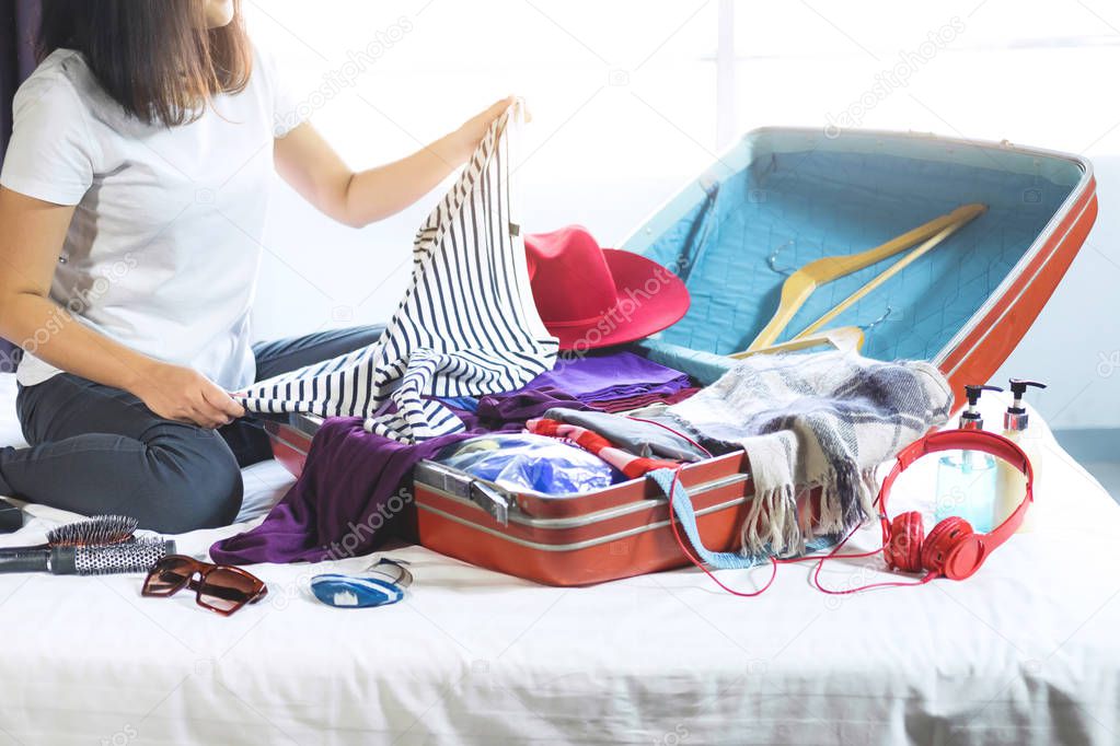 Travel and vacation concept, happiness young woman packing a lot of her clothes and stuff into suitcase on bed prepare for travel and journey trip in holiday.