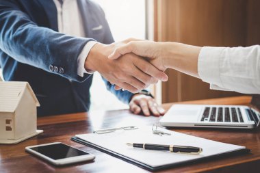 Emlakçı ve müşteriler el sıkışıyor. Ev sigortası, yatırım kredisi, tokalaşma ve başarılı anlaşmayla ilgili bitirilen sözleşmeyi kutluyorlar..