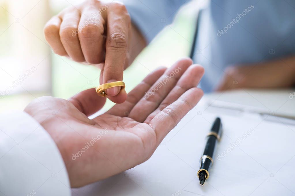 Husband and wife are signing decree of divorce (dissolution or cancellation) of marriage filing divorce papers and returning wedding ring.