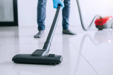 Temizlik ve ev işleri kavramı, bir elektrik süpürgesi katta evde kullanarak mavi kauçuk eldiven mutlu genç adam Temizleme.