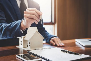 Emlakçı Satış Müdürü, kira kontratı ve konut sigortası için ipotek kredisi teklifiyle ilgili satış sözleşmesini imzaladıktan sonra müşterinin dosyalama anahtarlarını tutuyor..