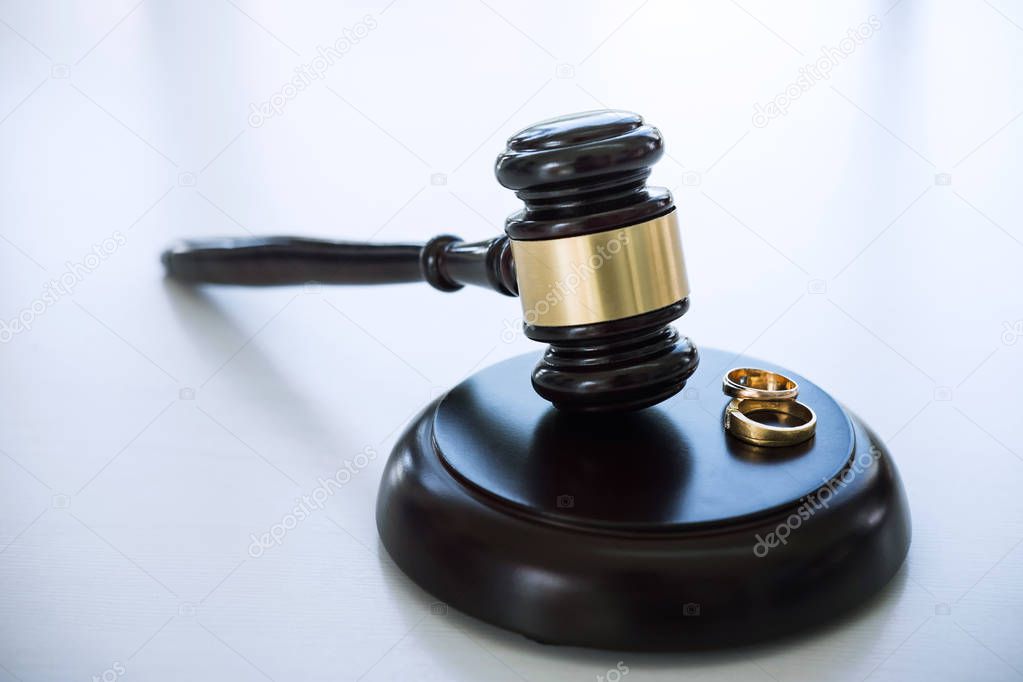 Close up of Judge gavel deciding on marriage divorce and two golden marriage ring.
