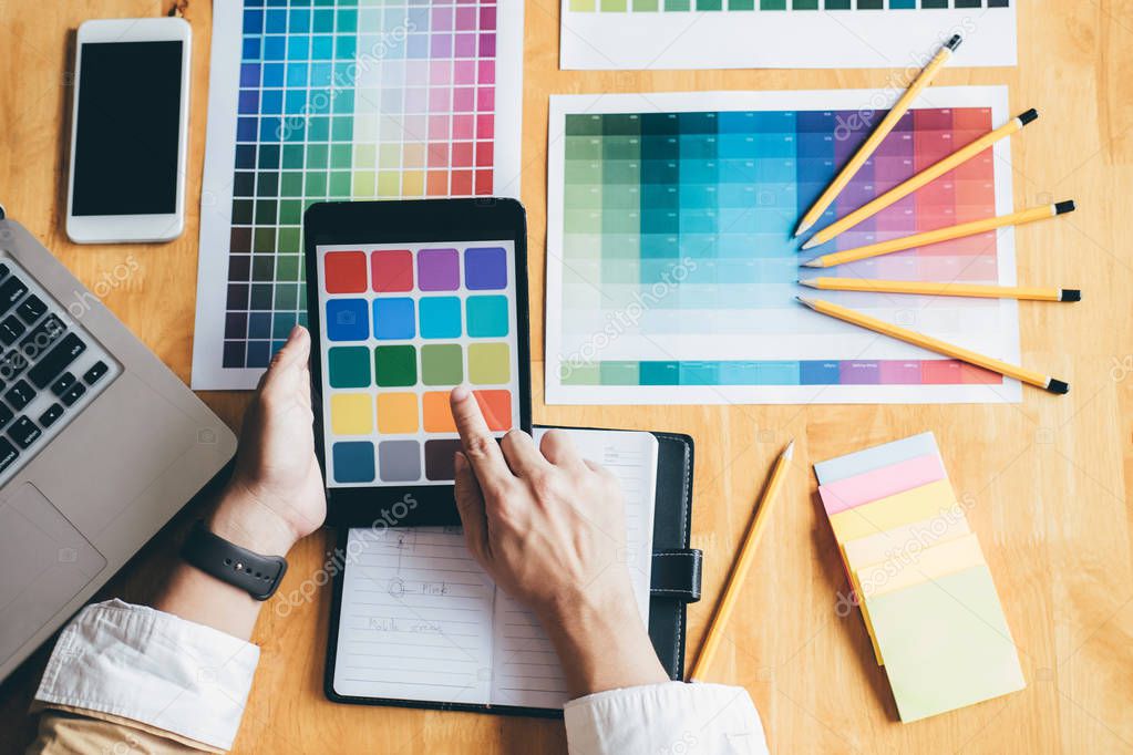 Young creative Graphic designer using graphics tablet to choosing Color swatch samples chart for selection coloring with work tools and accessories at workplace.