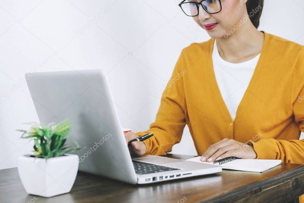 Happy casual young asian woman working in home or small office with using a laptop and document report on desk as a freelancer.