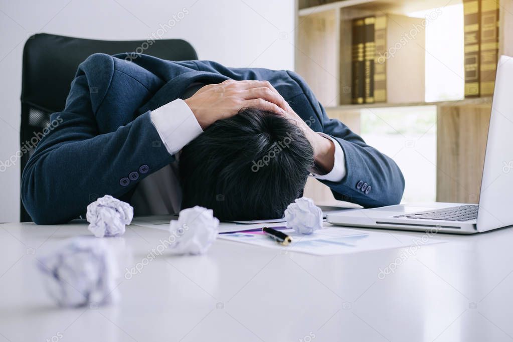 Feeling stress and headache, Businessman depressed and exhausted at his desk frustrated with problems with a pile of work while hiding his face on table.