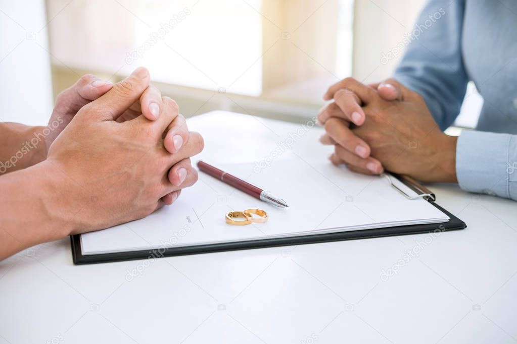 Husband and wife are reading divorce agreement and signing decree of divorce (dissolution or cancellation) of marriage filing divorce papers and two golden marry ring.