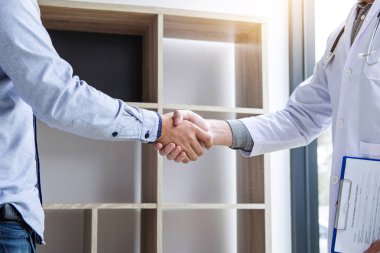 Tıp ve sağlık konsepti, beyaz önlüklü profesyonel erkek doktor başarılı tedavi yöntemleri önerdikten sonra hastayla tokalaşıyor.