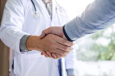 Tıp ve sağlık konsepti, beyaz önlüklü profesyonel erkek doktor başarılı tedavi yöntemleri önerdikten sonra hastayla tokalaşıyor.