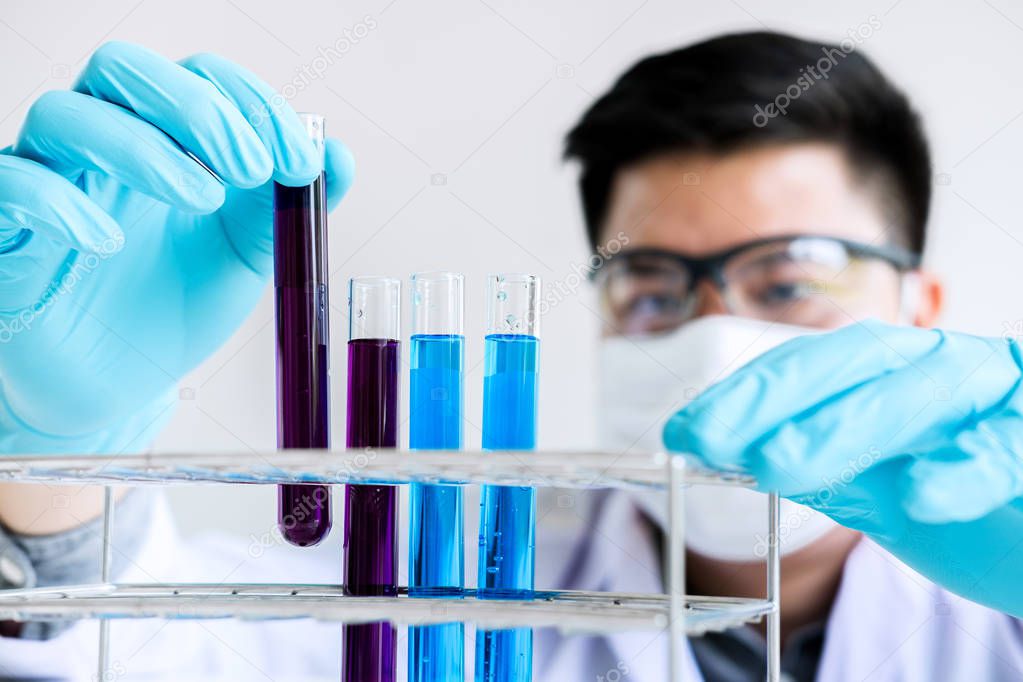Biochemistry laboratory research, Scientist or medical in lab coat holding test tube with reagent with drop of color liquid over glass equipment working at the laboratory.