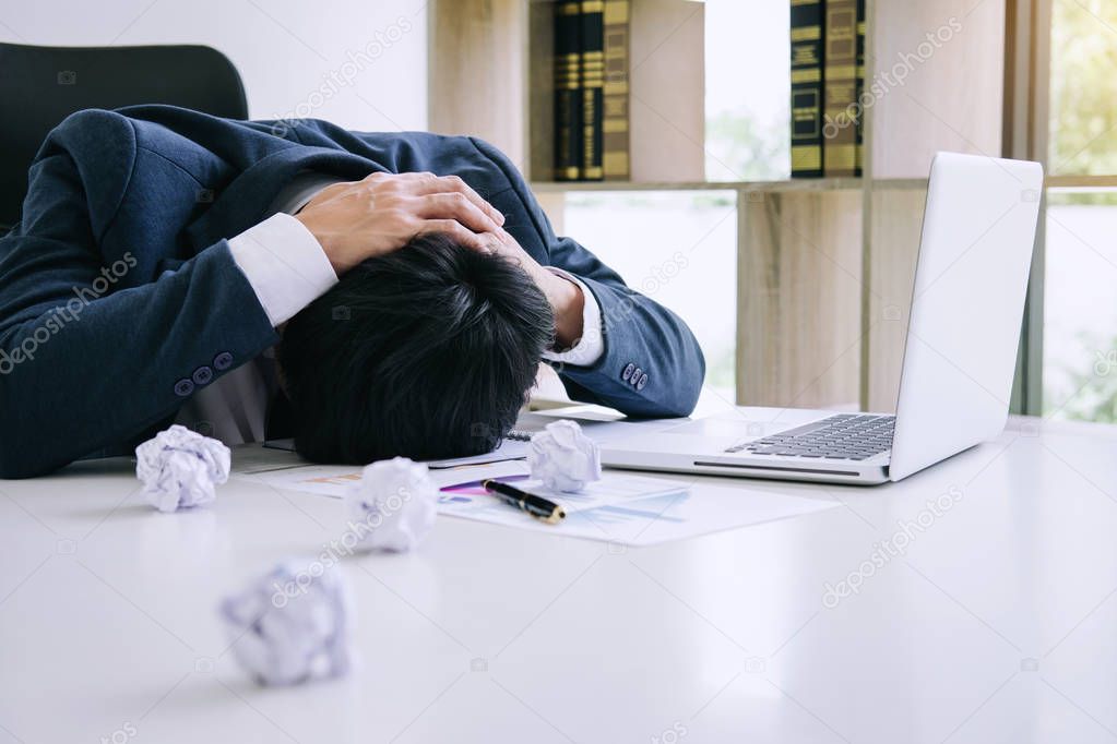Feeling stress and headache, Businessman depressed and exhausted at his desk frustrated with problems with a pile of work while hiding his face on table.