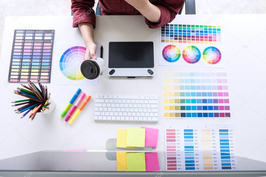 Image of female creative graphic designer working on color selection and drawing on graphics tablet at workplace, top view workspace.