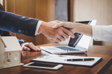 Emlakçı ve müşteriler el sıkışıyor. Ev sigortası, yatırım kredisi, tokalaşma ve başarılı anlaşmayla ilgili bitirilen sözleşmeyi kutluyorlar..