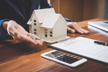 Emlakçı Satış Müdürü, kira kontratı ve konut sigortası için ipotek kredisi teklifiyle ilgili satış sözleşmesini imzaladıktan sonra müşterinin dosyalama anahtarlarını tutuyor..