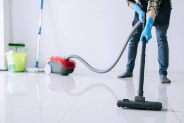 Temizlik ve ev işleri kavramı, bir elektrik süpürgesi katta evde kullanarak mavi kauçuk eldiven mutlu genç adam Temizleme.