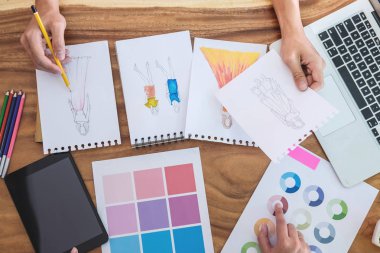 İki genç profesyonel moda tasarımcısı meslektaşları çalışma ve işyeri dizüstü bilgisayar, dijital tablet ve renk şemaları, moda tasarımcısı şık konsept çizimler giyim için çizim proje.