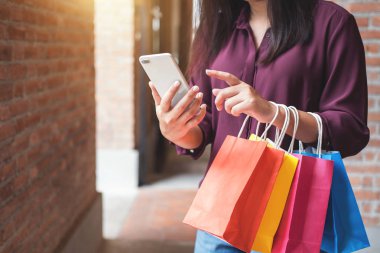 Tüketim, alışveriş, yaşam kavramı, Genç kadın holding renkli alışveriş torbaları ve akıllı telefon Alışveriş keyfi.