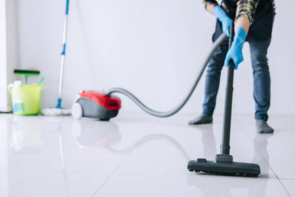 Housekeeping and housework cleaning concept, Happy young man in blue rubber gloves using a vacuum cleaner on floor at home.