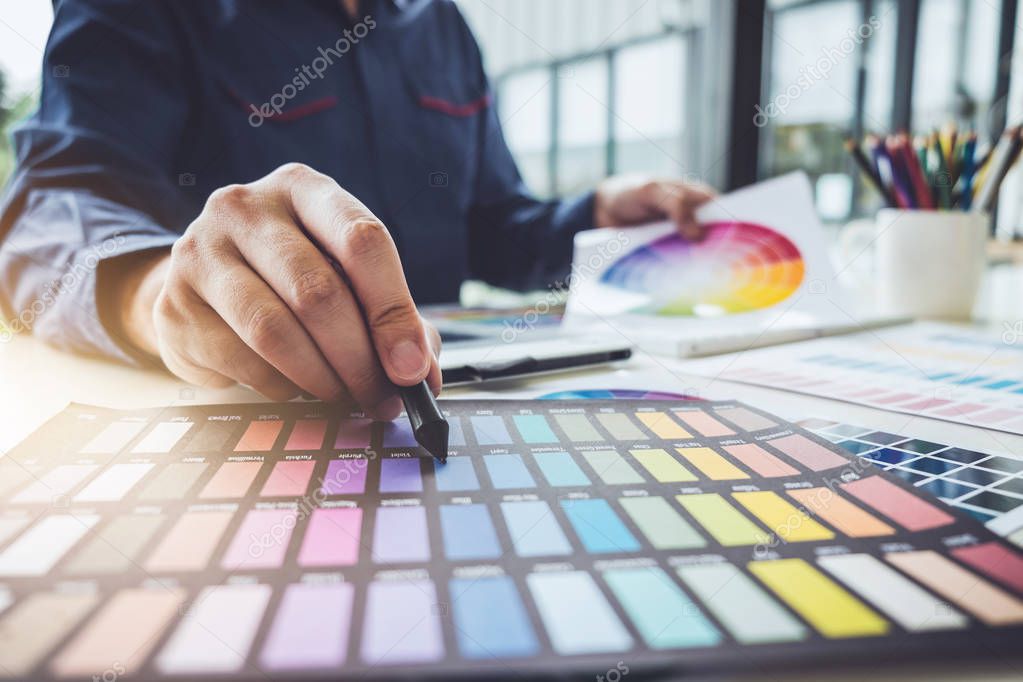 Image of male creative graphic designer working on color selection and drawing on graphics tablet at workplace with work tools and accessories.