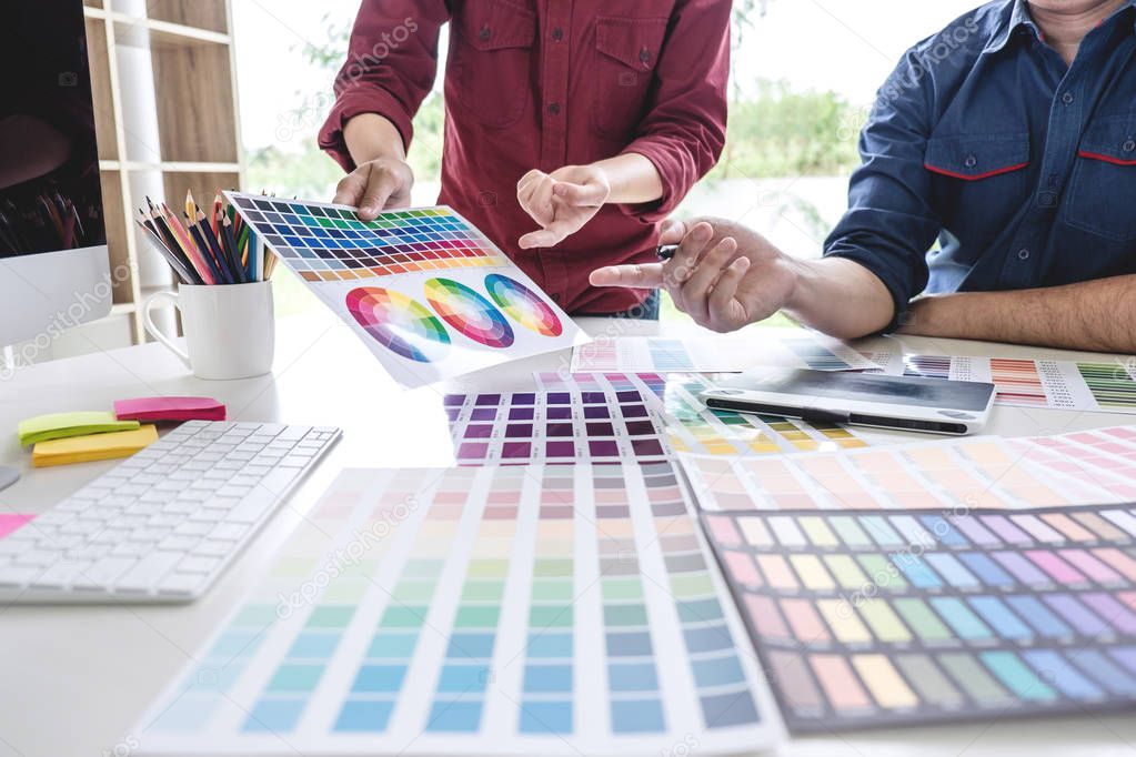 Two colleagues creative graphic designer working on color selection and drawing on graphics tablet at workplace.