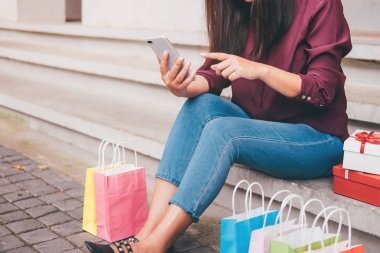 Tüketim, alışveriş, yaşam kavramı, smartphone alışveriş zevk oynarken alışveriş torbaları ve hediye kutusu yakın oturan genç kadın.