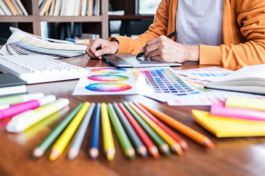 İş yerinde iş araçları ve aksesuarlarıyla renk seçimi ve grafik tableti üzerinde çalışan kadın yaratıcı grafik tasarımcı resmi.