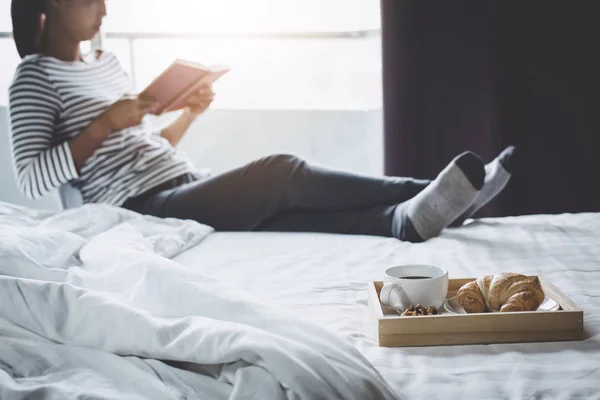 休闲和娱乐 年轻快乐的女人在床上享受阅读老书在假日和早晨的咖啡和牛角面包 — 图库照片