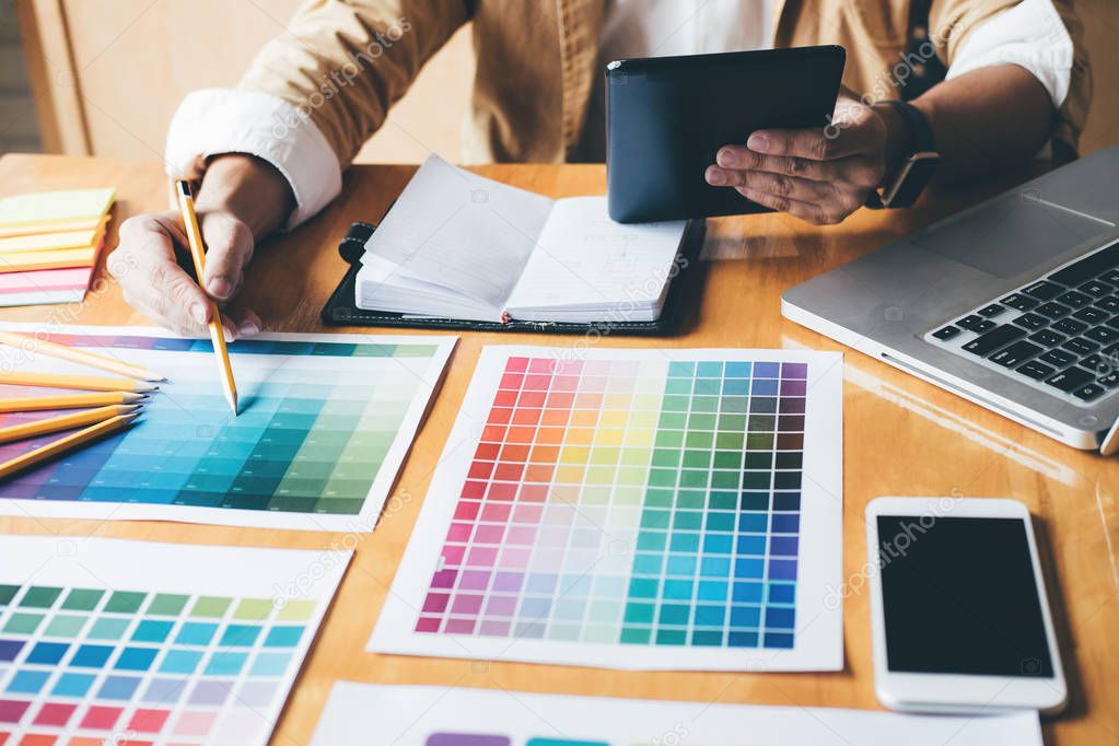 Young creative Graphic designer using graphics tablet to choosing Color swatch samples chart for selection coloring with work tools and accessories at workplace.