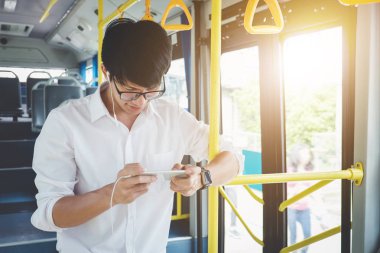 Küçük Asya adam video izle smartphone kullanarak veya gülümseme mutlu, ulaşım, turizm ve road trip kavramı ile oyun oynarken bir otobüste ayakta gezgin.