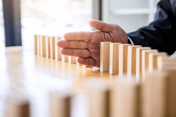 Wooden game strategy, Businessman hand stopping falling wooden dominoes effect from continuous toppled or risk, strategy and successful intervention concept for business.