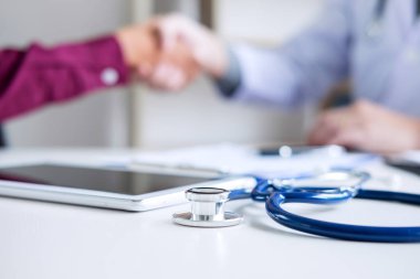 Beyaz önlüklü profesyonel erkek doktor, başarılı tedavi yöntemleri, ilaç ve sağlık konsepti önerdikten sonra kadın hastayla el sıkışıyor..