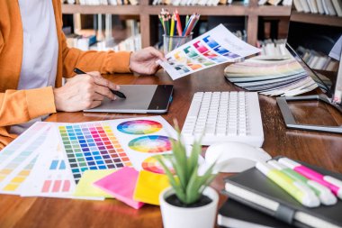 İş yerinde iş araçları ve aksesuarlarıyla renk seçimi ve grafik tableti üzerinde çalışan kadın yaratıcı grafik tasarımcı resmi.
